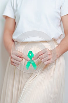 Woman holding Teal Ribbon on abdomen for January Cervical Cancer Awareness month. Uterus and Ovaries, Cervix, Endometriosis,