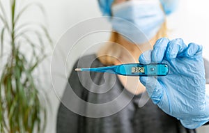 Woman holding thermometer in hand with protectice glove. Fever and colds concept