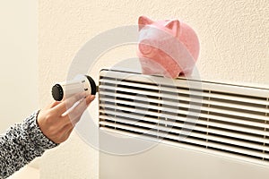 Woman holding thermostat near piggy bank on calorifer. Heating saving concept