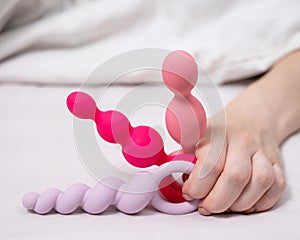 Woman holding three different anal beads while lying in bed.