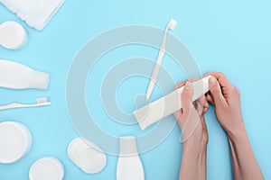 Woman holding toothbrush and toothpaste isolated on blue with cosmetic cream and lotion bottles