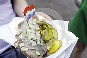 Woman holding traditional Dutch snack with raw herring with pickles