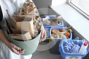 Woman holding trash bin with paper garbage indoors