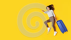 Woman Holding Travel Suitcase Pointing At Copy Space, Yellow Background