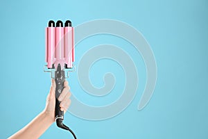 Woman holding triple curling hair iron on light blue background, closeup. Space for text