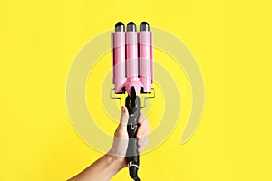 Woman holding triple curling hair iron on yellow background, closeup