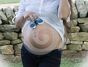A woman holding two blue shoes on her belly for her unborn son