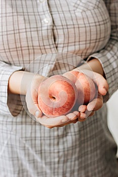 Woman holding two ripe peaches in her hands.