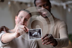 Woman holding ultrasound image of her baby showing her husband details on it.