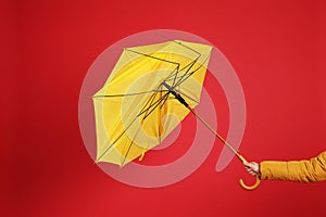 Woman holding umbrella caught in gust of wind on red background