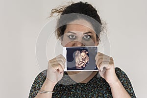 Woman holding unborn baby sonography image in hands, in front of