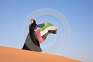 Woman holding the United Arab Emirates flag in the desert.