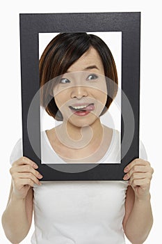 Woman holding up a black picture frame, sticking her tongue out