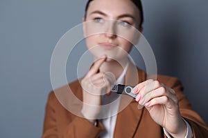 Woman holding usb flash drive against grey background, focus on hand