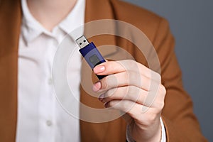 Woman holding usb flash drive against grey background, focus on hand