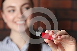 Woman holding usb flash drive near brick wall, focus on hand