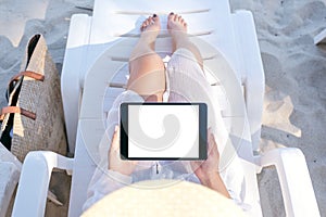 A woman holding and using a black tablet pc with blank desktop screen while laying down on beach chair on