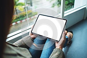 A woman holding and using digital tablet with blank white desktop screen while sitting on the floor