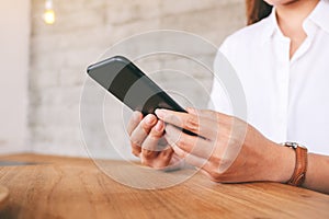 A woman holding , using and looking at smart phone on wooden table