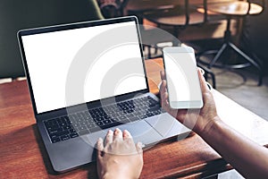 Woman holding and using mockup mobile phone with blank white screen and laptop on wooden table in cafe