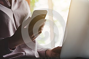 Woman holding and using smart phone, touching screen and working on laptop