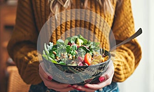 Woman holding a vegetable salad bowl near window light.