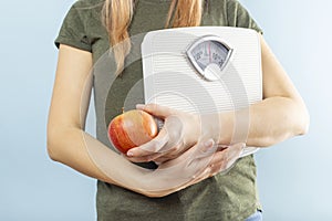 A woman holding weight scales and red apple on a blue background. Healthy eating concept. Diet