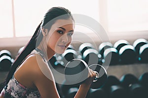 Woman holding weight to train her arm and shoulder muscles in fitness gym