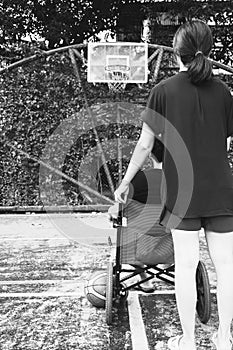 Woman holding wheel chair with with sitting man at basketball c