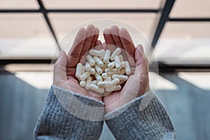 A woman holding white medicine capsules in hand