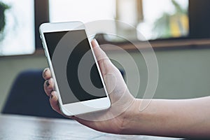 A woman holding white mobile phone with blank black screen on wooden table