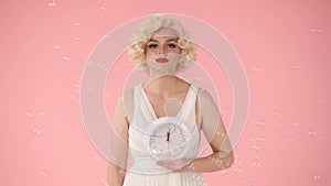 Woman holding a white round wall clock in her hand. Woman in image on Marilyn Monroe, in studio surrounded by soap