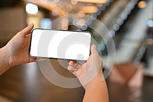 A woman holding a white screen mobile phone over blurred shopping mall background