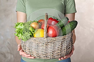 Woman holding wicker basket with ripe fruits and vegetables on color background