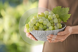 Woman holding wicker bowl with ripe juicy grapes, closeup