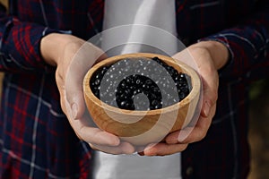 Woman holding wooden bowl of bilberries, closeup