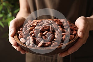 Woman holding wooden bowl of cocoa beans, closeup