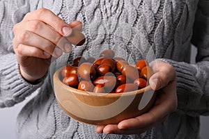 Woman holding wooden bowl with fresh Ziziphus jujuba fruits on light background, closeup