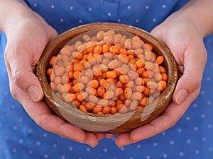 Woman holding wooden bowl full of frozen ripe sea buckthorn berries in her hands