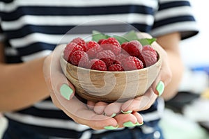 Woman holding wooden bowl with raspberries, cloce up