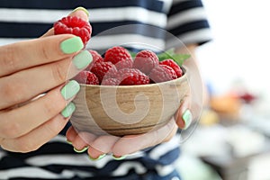 Woman holding wooden bowl with raspberries, cloce up