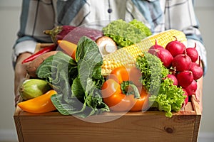 Woman holding wooden crate full of fresh vegetables on light background, closeup
