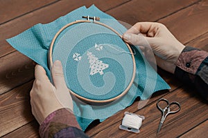 Woman holding wooden hoop with cross-stitch pattern and needle in her hands