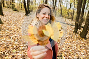 Woman holding yellow autumn leaves in the forest