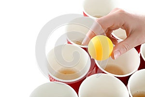 Woman holding yellow ball over cups arranged for playing beer pong, closeup