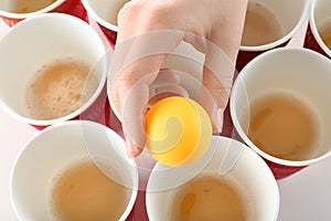 Woman holding yellow ball over cups arranged for playing beer pong, closeup