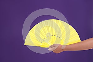 Woman holding yellow hand fan on purple background, closeup