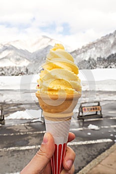 Woman holding yellow softcream with snow background.
