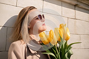 Woman holding yellow tulips, leaning against stone wall. Women& x27;s holiday concept, giving flowers.