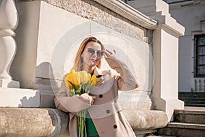 Woman holding yellow tulips, leaning against stone wall. Women& x27;s holiday concept, giving flowers.